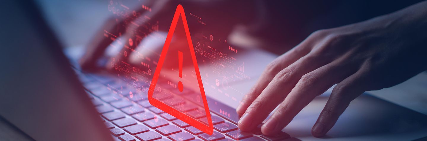 Hande tippen auf einer Laptop-Tastatur. Darpber schwebt das Hologram eines Warnsymbols.